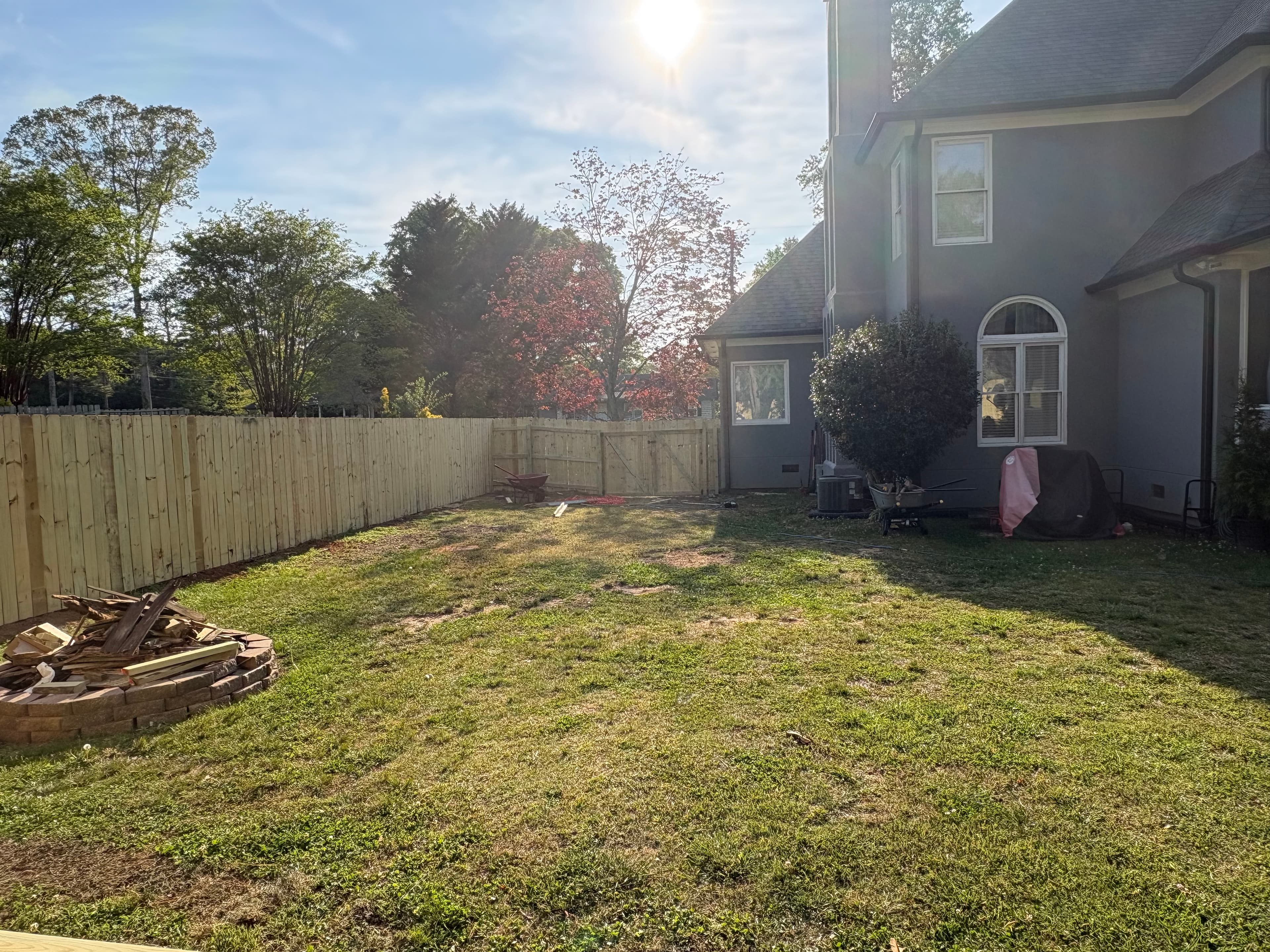 Grassy backyard featuring a new wooden fence, grey house, and a stone fire pit.