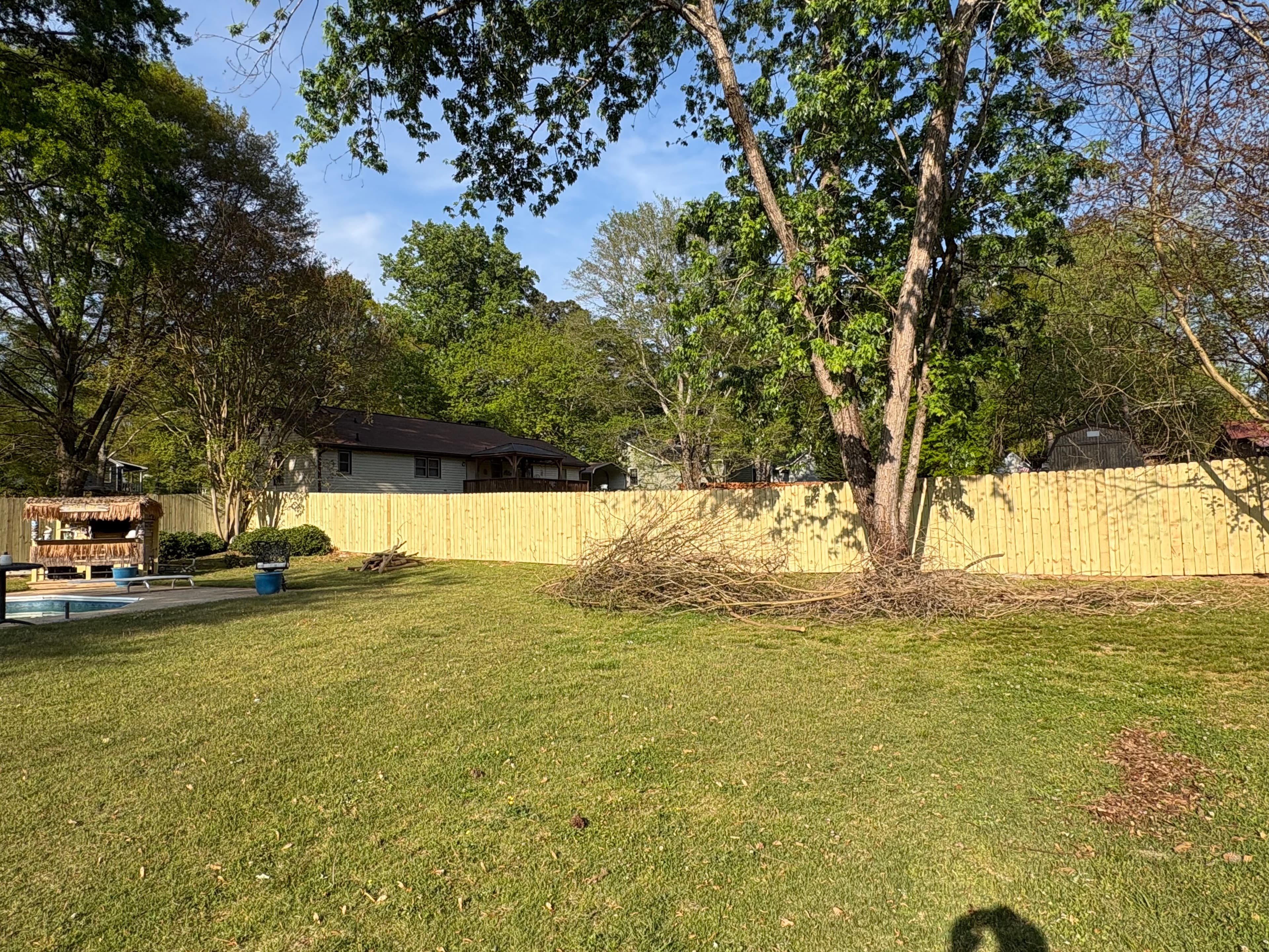 Grassy backyard with a wooden fence, a large brush pile, and a tiki bar.