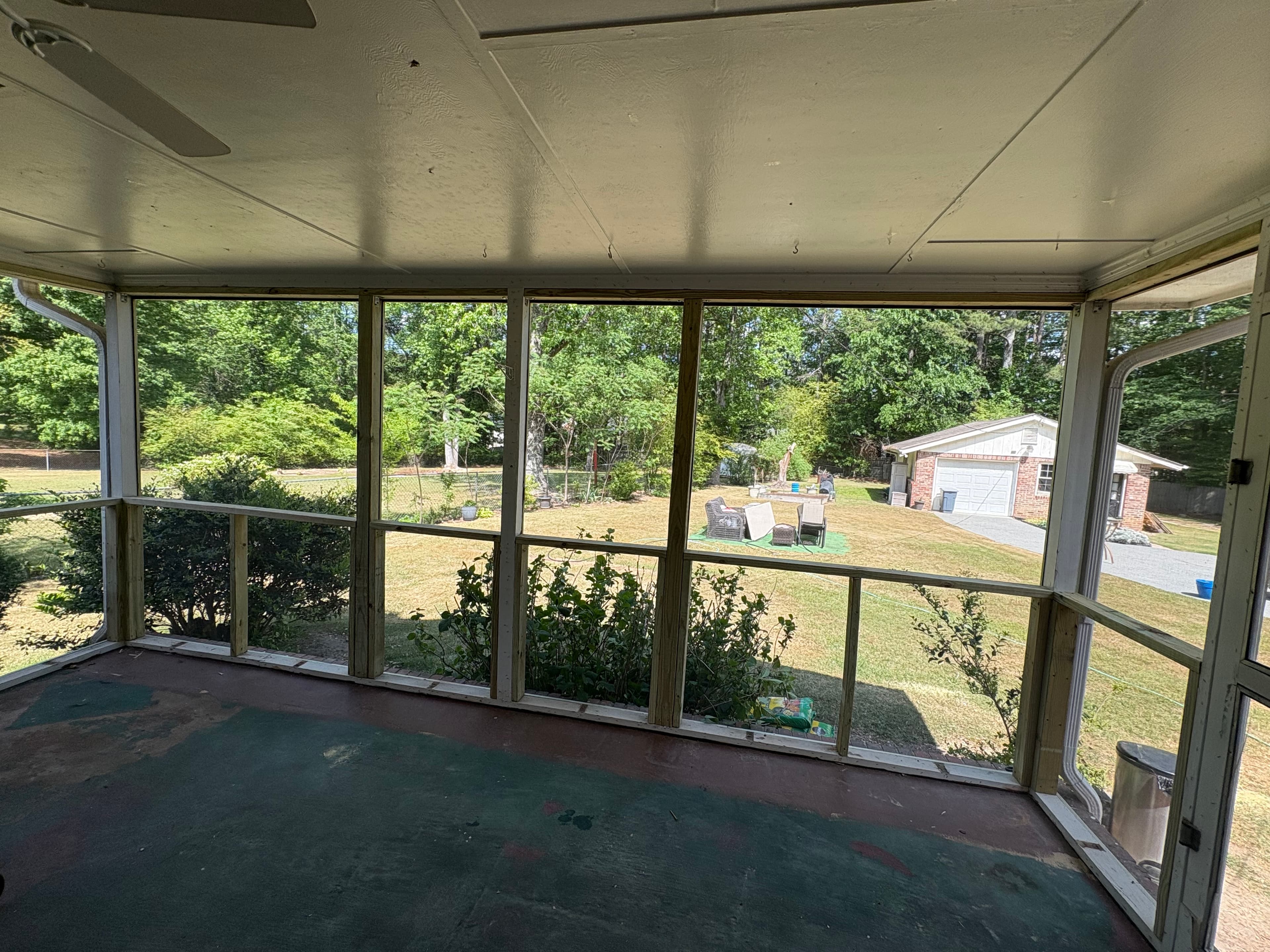 View from a screened porch overlooking a grassy backyard with trees and a white garage.