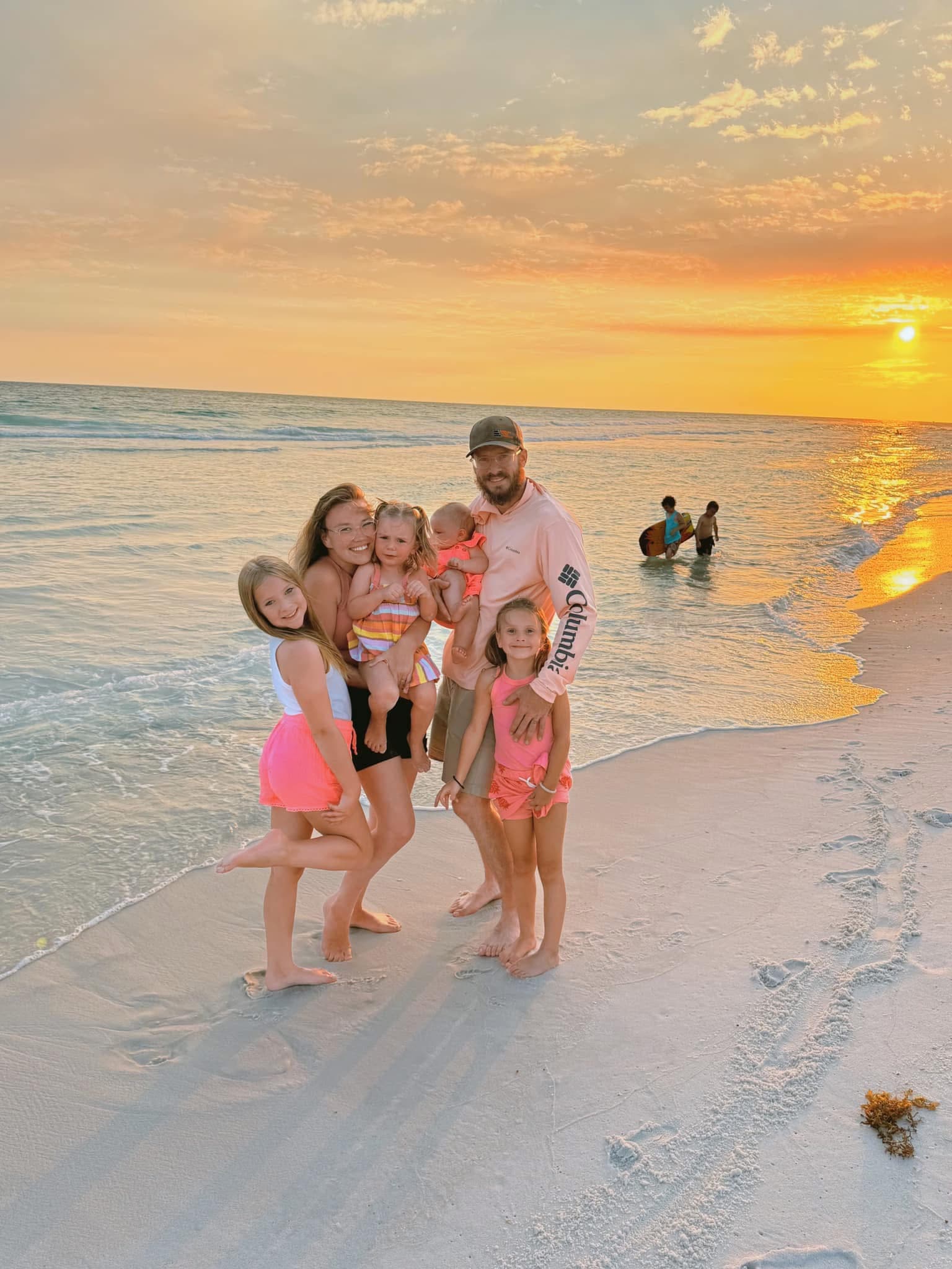 Family of six posing on a sandy beach during a vibrant sunset over the ocean.